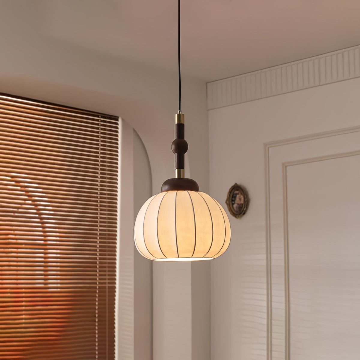 Clérachic silk globe pendant lamp lit in a corner beside amber window blinds, an arched opening and a panelled door behind it.