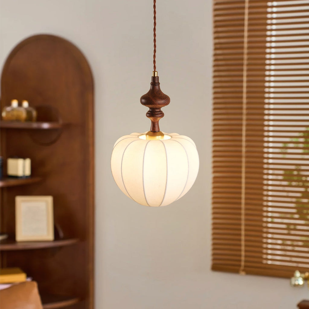 Close-up of a Clérachic pendant with a lit, ribbed white shade and a turned wooden top, beside wooden slatted blinds.