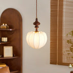 Close-up of a Clérachic pendant with a lit, ribbed white shade and a turned wooden top, beside wooden slatted blinds.