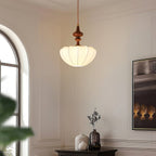 A Clérachic pendant lit in a pale room with an arched window, its ribbed white shade glowing under a turned wooden top.