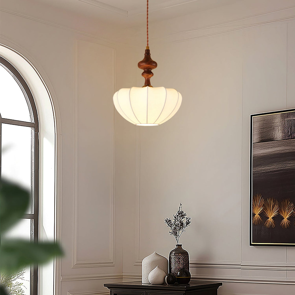 A Clérachic pendant lit in a pale room with an arched window, its ribbed white shade glowing under a turned wooden top.