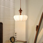 Ribbed white silk shade of a Clérachic pendant glowing in a corner beside slatted blinds, with a small clock below.