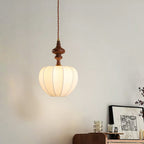 A Clérachic pendant with a rounded, lit shade and a slim wooden top, hung above a walnut sideboard with framed art.