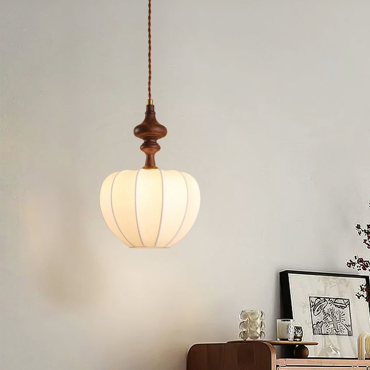 A Clérachic pendant with a rounded, lit shade and a slim wooden top, hung above a walnut sideboard with framed art.