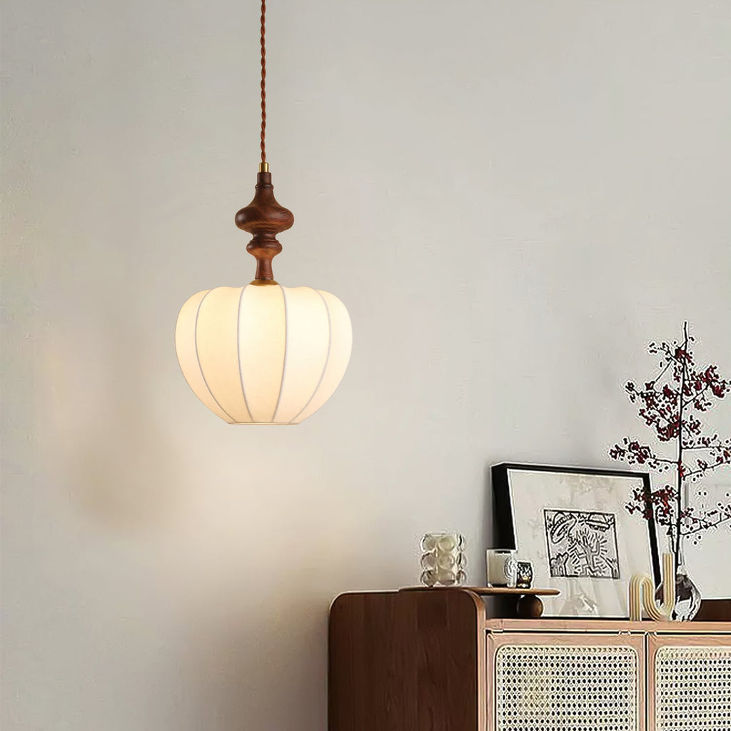 Smaller rounded white shade on a Clérachic pendant, glowing above a sideboard with a rattan front and a vase of branches.