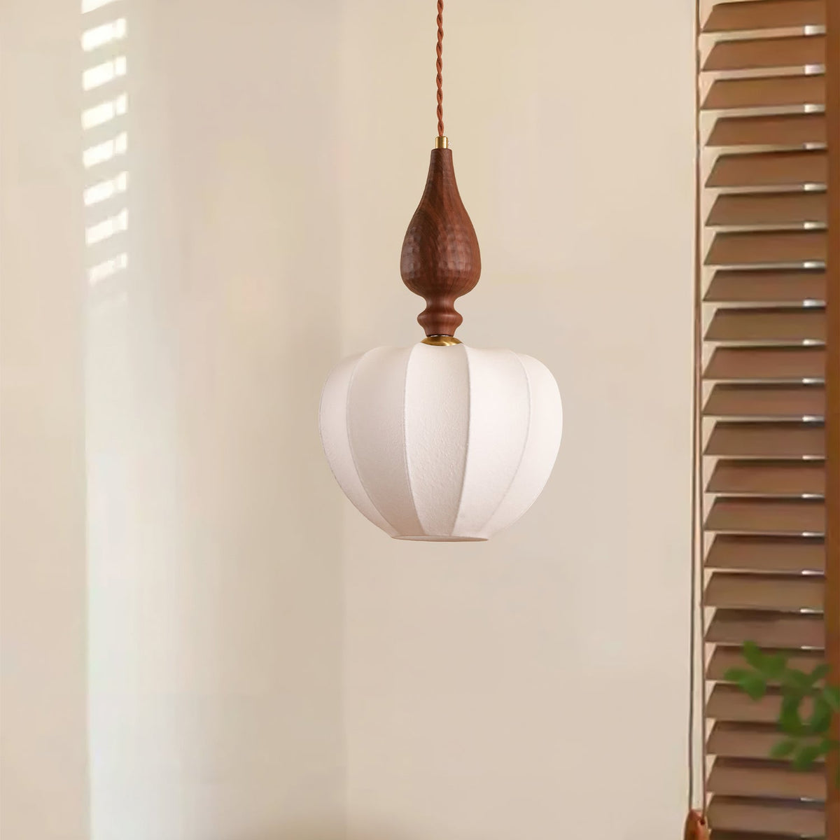 An unlit Clérachic pendant with a rounded white shade and a dark wooden top, next to wooden louvred shutters.