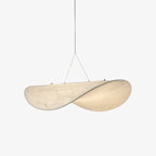 A white, softly twisted, leaf-shaped pendant hangs from two fine cables against a plain pale backdrop, shown as this Clérachic silk pendant.