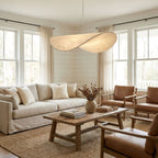 A twisted white shade glows softly above a cream sofa and wooden coffee table, between tall windows, in a living room with this Clérachic pendant.