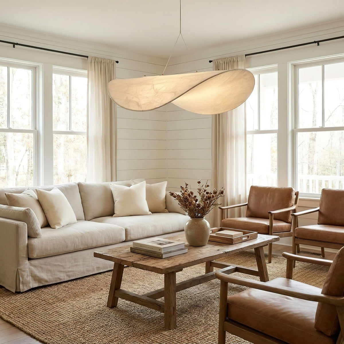 A twisted white shade glows softly above a cream sofa and wooden coffee table, between tall windows, in a living room with this Clérachic pendant.