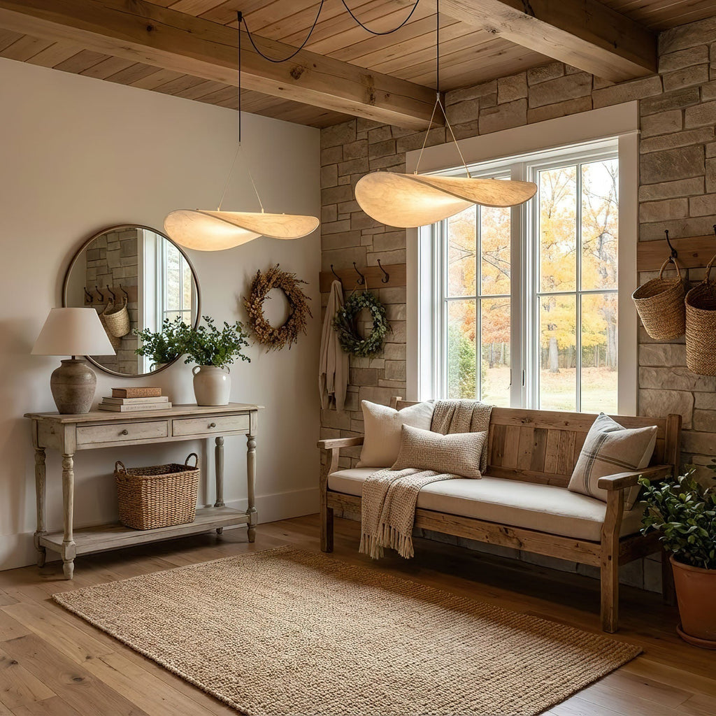 Two twisted white shades hang near a stone wall and a timber ceiling above a bench with cushions and a round mirror, from Clérachic.