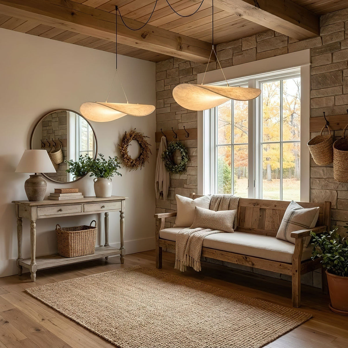 Two twisted white shades hang near a stone wall and a timber ceiling above a bench with cushions and a round mirror, from Clérachic.