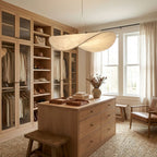A twisted white pendant glows above a wooden island in a walk-in wardrobe with glass-fronted cabinets, shown as a Clérachic pendant.