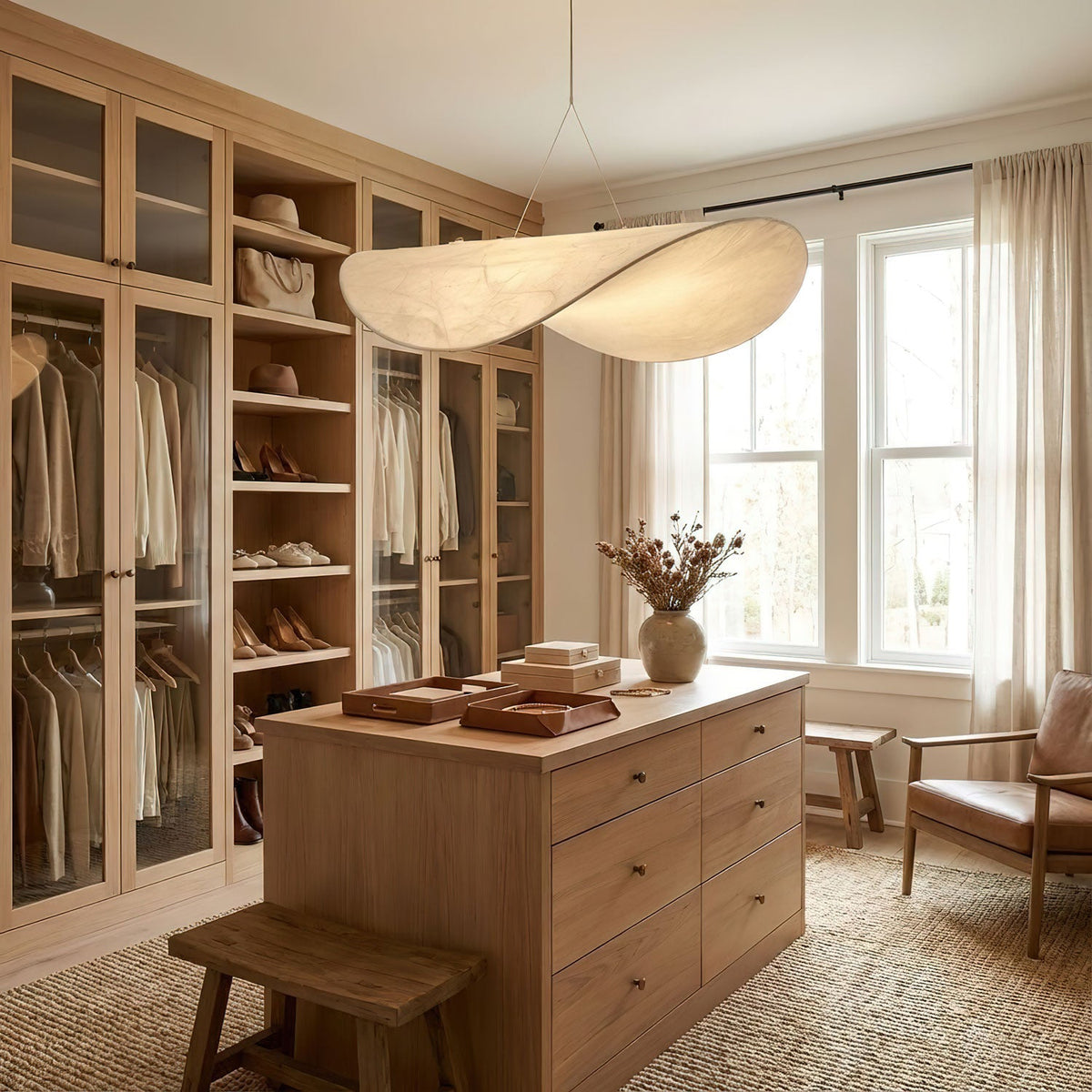 A twisted white pendant glows above a wooden island in a walk-in wardrobe with glass-fronted cabinets, shown as a Clérachic pendant.