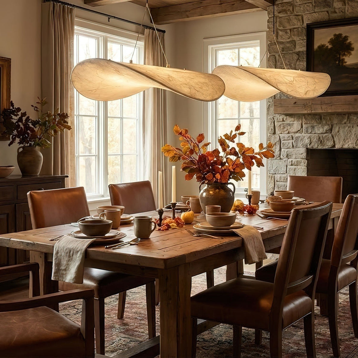 Two twisted white pendants hang above an autumn dining table with leather chairs and a stone fireplace wall, from Clérachic.