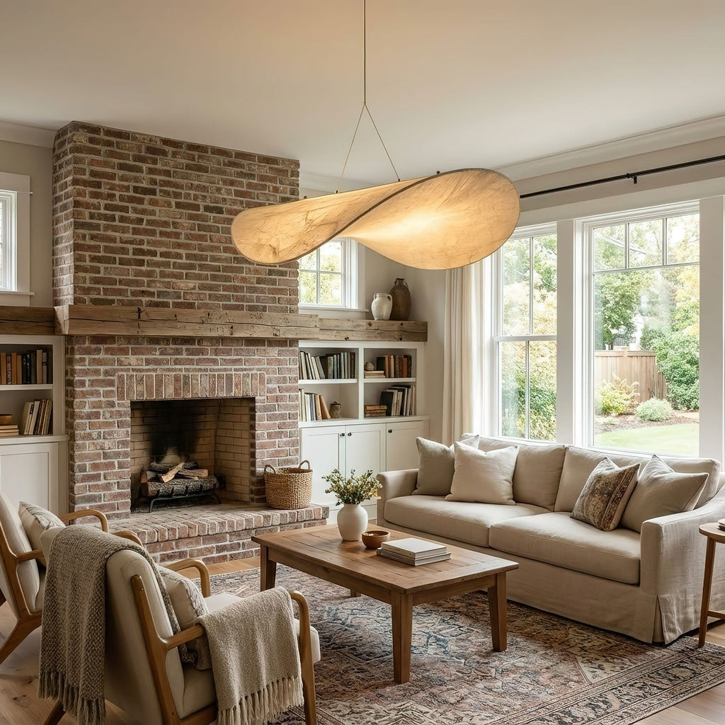 A twisted white pendant hangs in a living room with a brick fireplace, a cream sofa and an armchair with a throw, from Clérachic.