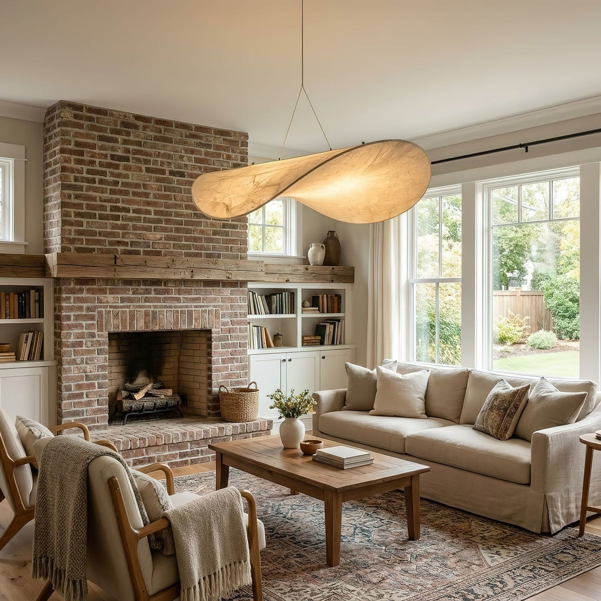 A twisted white pendant hangs in a living room with a brick fireplace, a cream sofa and an armchair with a throw, from Clérachic.