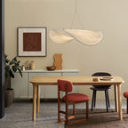 A twisted white pendant hangs over a pale oak dining table with a red-cushioned chair, beside a framed print and a low sideboard, from Clérachic.