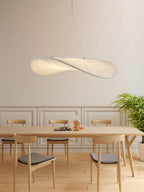 A twisted white pendant hangs above a long pale oak table with light chairs, in front of a panelled wall and a green plant, from Clérachic.