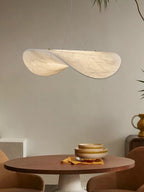 A twisted white pendant hangs against a beige wall above a round walnut table set with stacked bowls, from Clérachic.