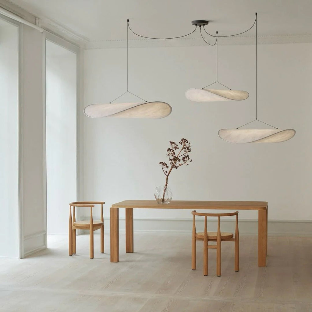 Three twisted white pendants hang at different heights above an oak dining table in a pale room with tall windows, from Clérachic.