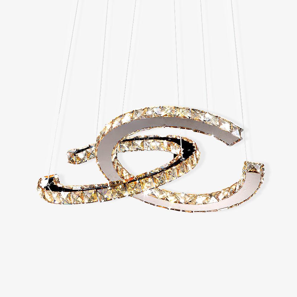 Two interlocking crescent rings of cognac-toned crystal on polished steel, a Clérachic pendant hung from fine cables on a white backdrop.