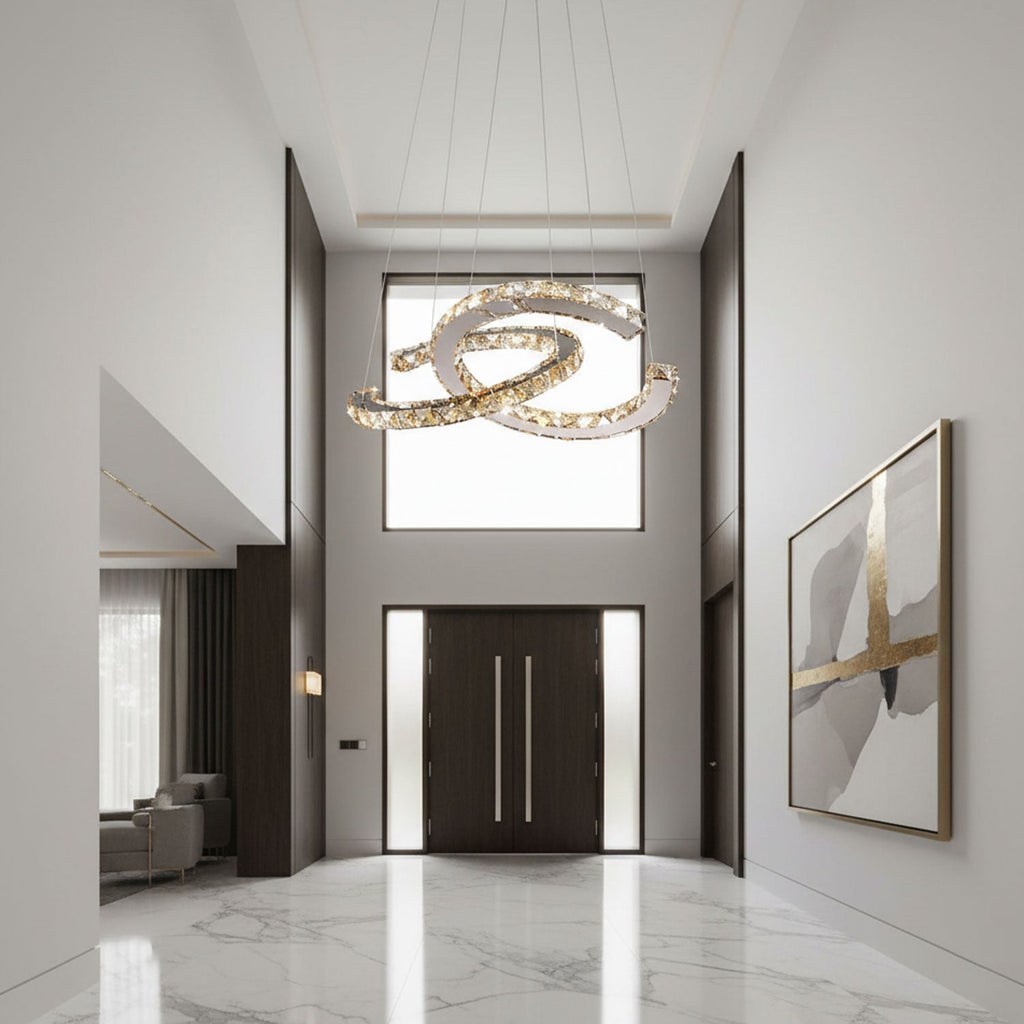 A Clérachic crystal pendant of two crossed crescents hangs in a tall white entrance hall, above a marble floor and dark double doors.