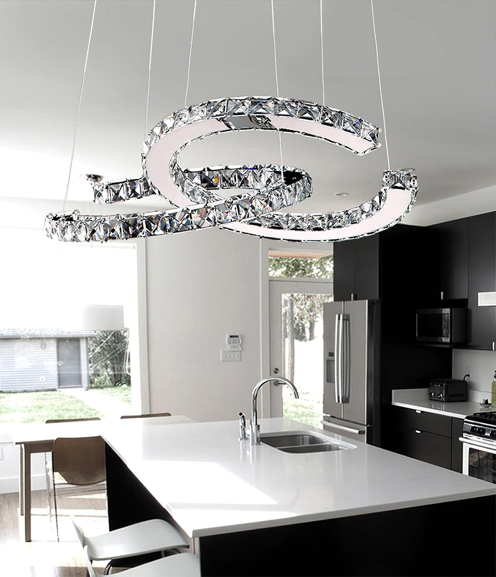Clear crystal Clérachic pendant over a white kitchen island with a sink, in front of dark cabinets and a steel fridge.