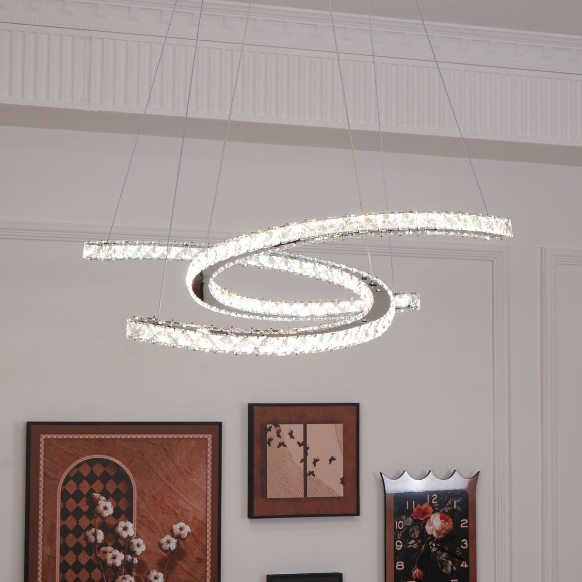 Lit Clérachic crystal pendant in a cool white tone, hung against a white panelled wall with framed prints below.