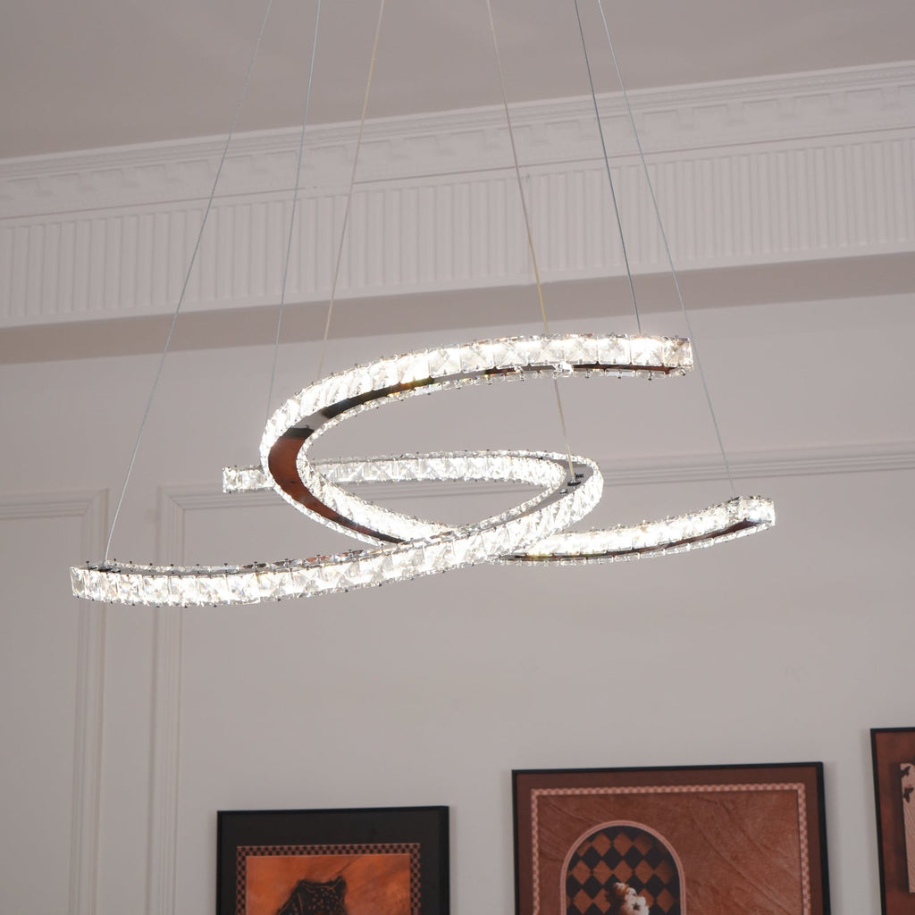 Clérachic pendant with two crystal crescents, lit cool white, hanging below a ceiling cornice with framed prints beneath.