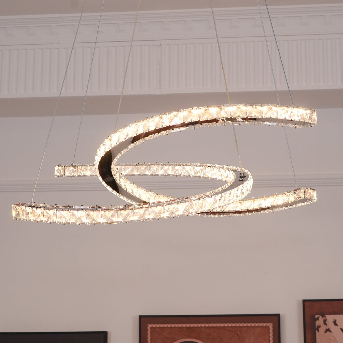 Clérachic crescent pendant glowing a warm amber, seen from below, with panelled walls and framed prints behind it.