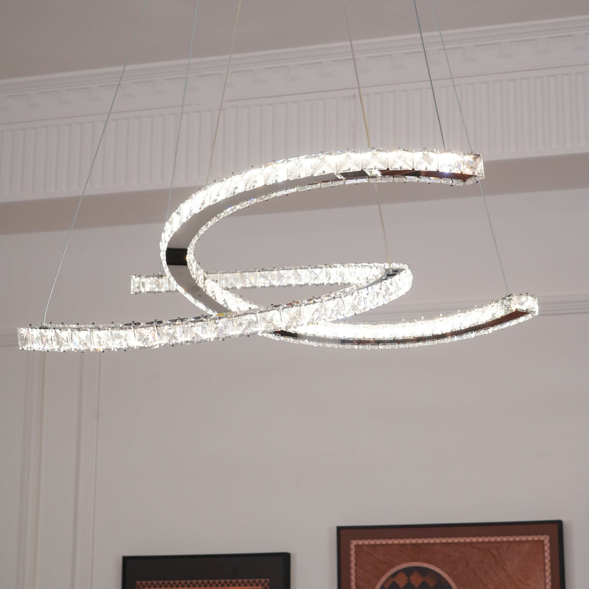 Side view of the lit Clérachic pendant, its steel crescents trimmed with crystals and hung by thin cables.