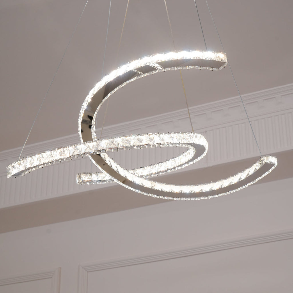Low angle on the Clérachic crystal pendant lit, one crescent passing through the other, with a cornice above.