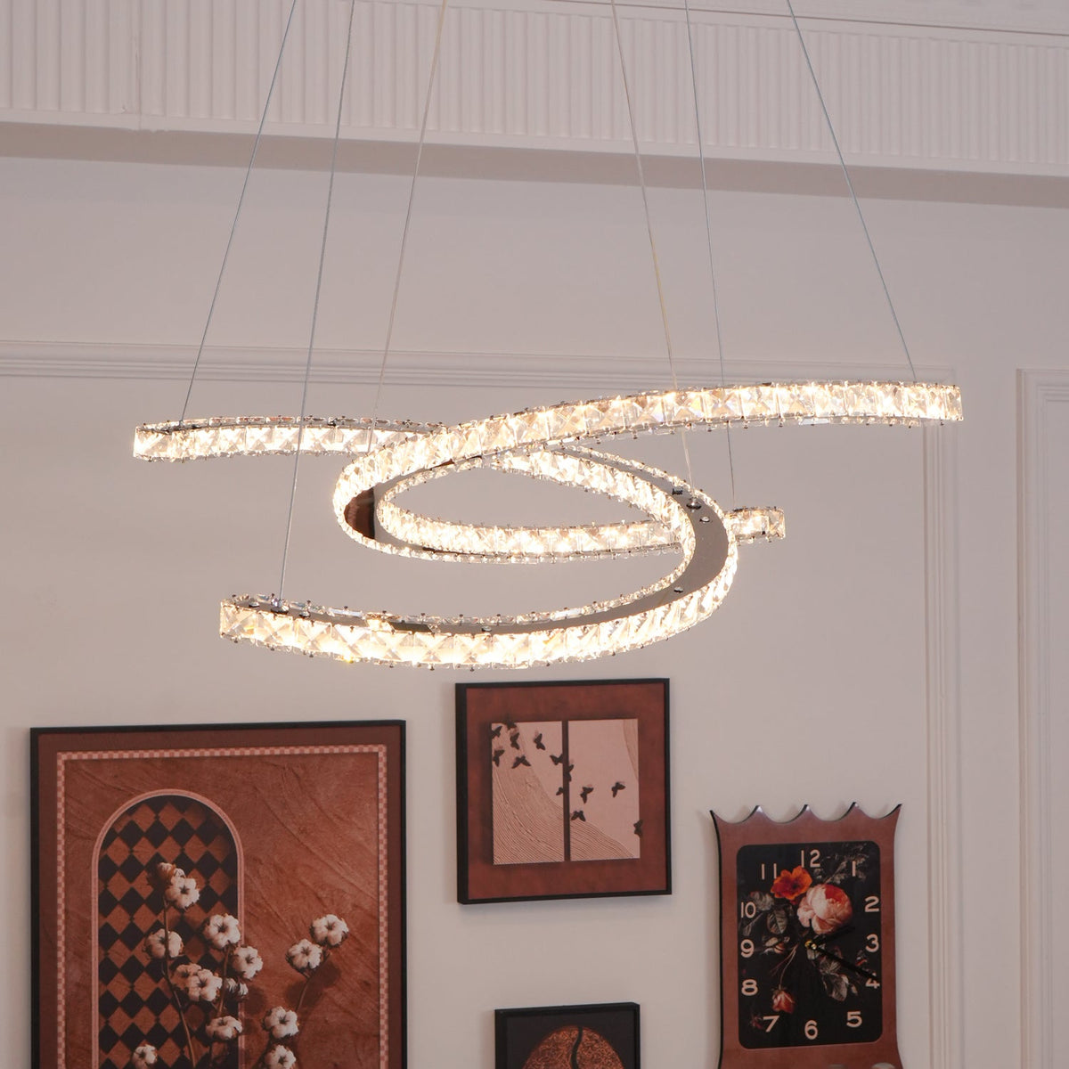 Warm-lit Clérachic crescent pendant in a white room, with a gallery of framed pictures and a clock on the wall below.