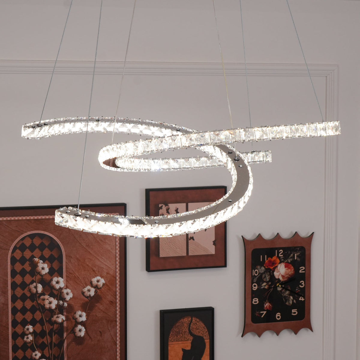 Lit Clérachic pendant close to the camera, with framed pictures and a clock on the white wall beneath.