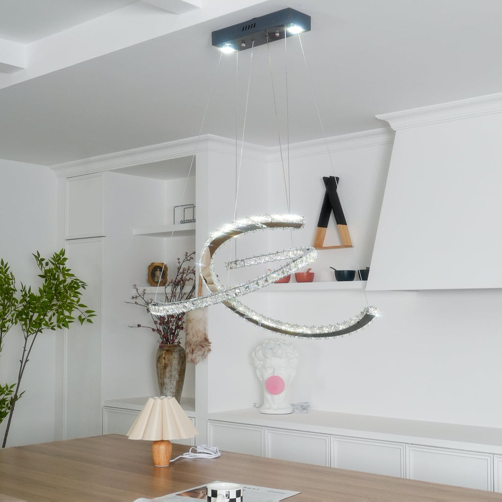 Crystal crescent pendant from Clérachic below a dark canopy, with a leafy plant and a white shelving wall behind.