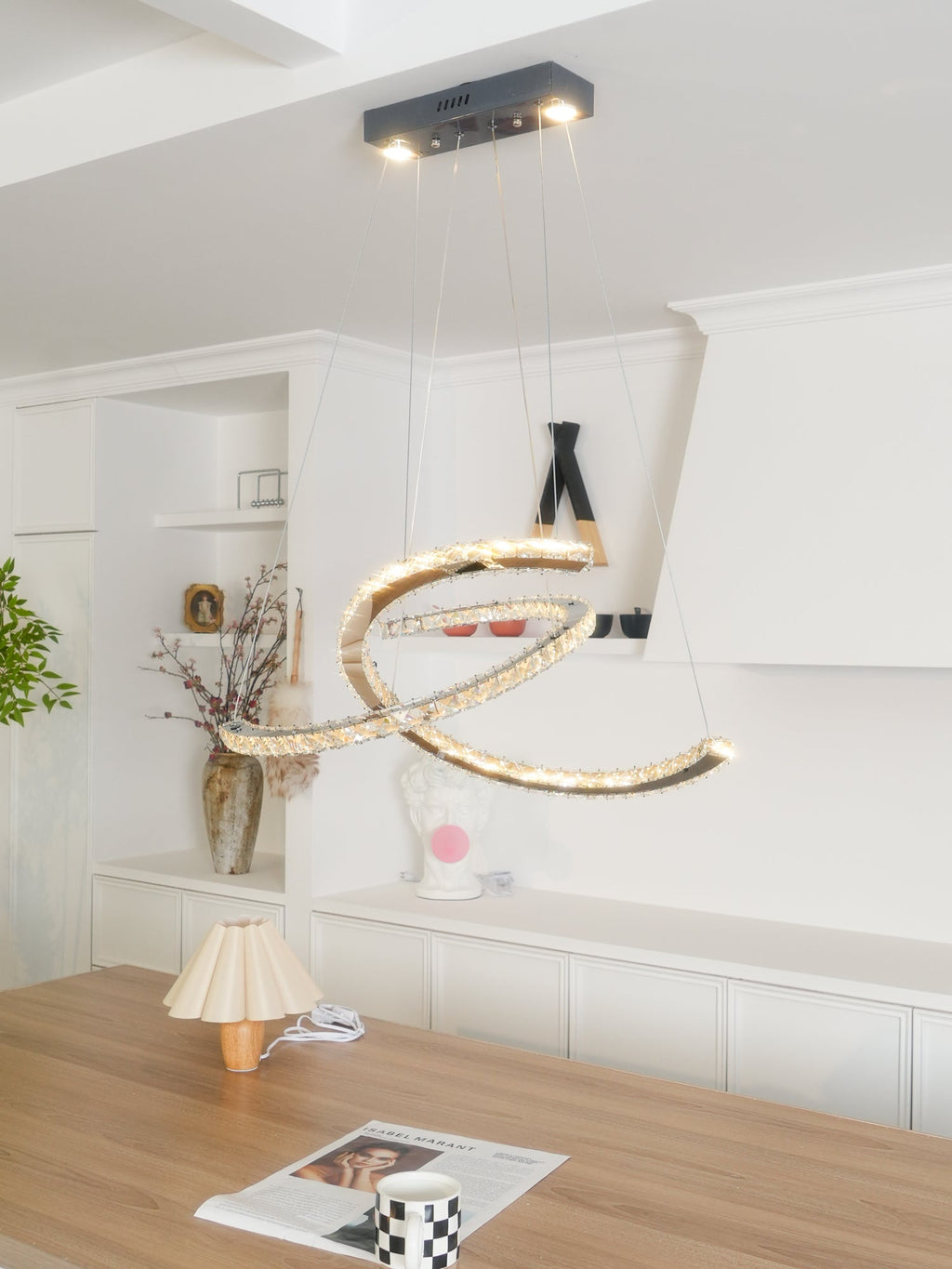 Clérachic crescent pendant glowing warm under a dark canopy, with a table lamp and a plaster head in a white room.