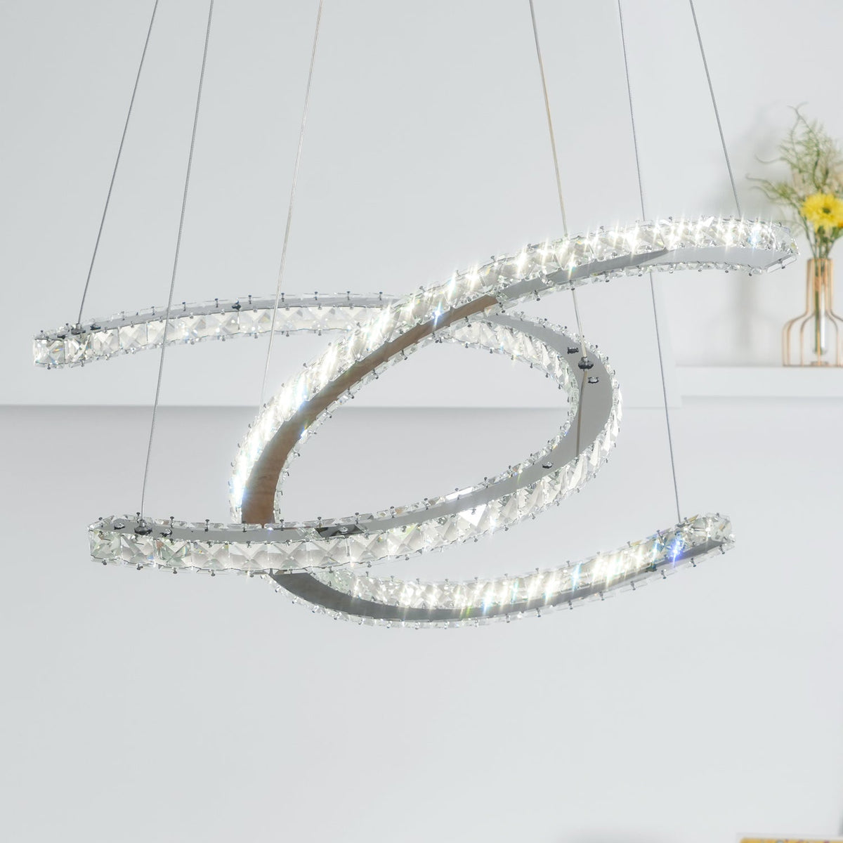 Close, upward view of the Clérachic pendant lit, its crystal-edged crescents crossing against a pale wall.