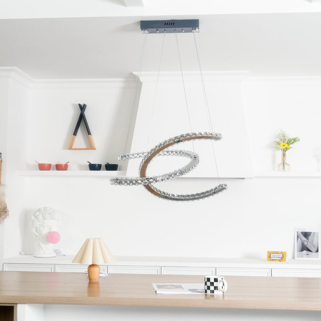 Distant view of the Clérachic crescent pendant, unlit, in a white room with shelves, a table lamp and a wooden counter.