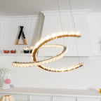 Clérachic pendant lit warm, its crystals glittering along both crescents, in front of a white shelving wall.