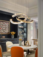 Clérachic crescent pendant lit above a round marble dining table with orange chairs, in a room with navy shelving.