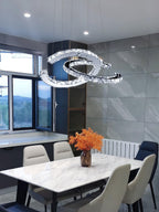 Clear-crystal Clérachic pendant above a marble-look table, with cream chairs and a window in a grey tiled room.