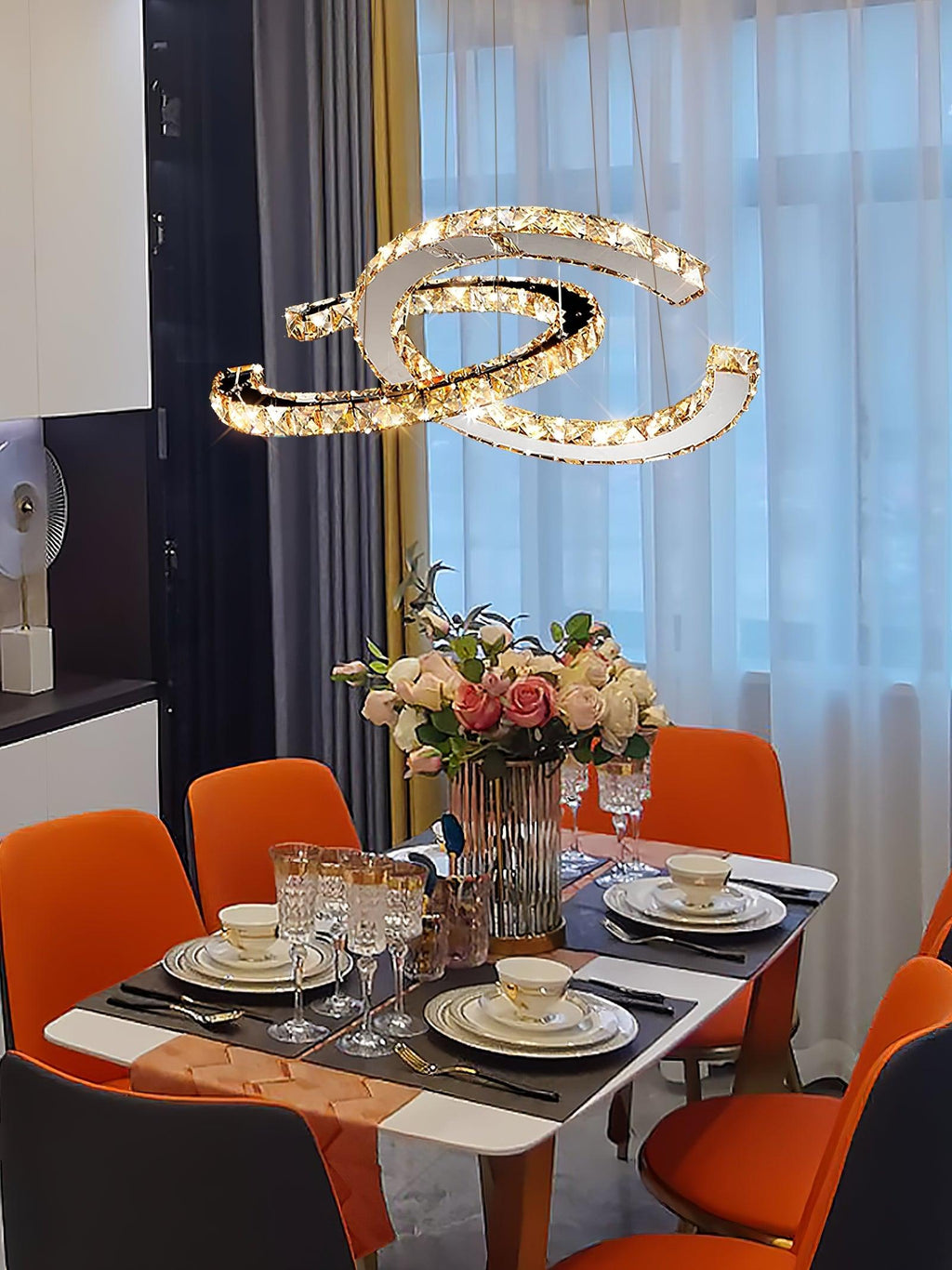 Warm-lit Clérachic pendant above a laid dining table with orange chairs, flowers and place settings.