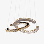 Clérachic crystal pendant with cognac-toned stones, lit and hanging from thin cables on a plain pale backdrop.