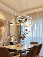 Clérachic crescent pendant lit warm above a marble-top dining table with brown leather chairs and sheer curtains.