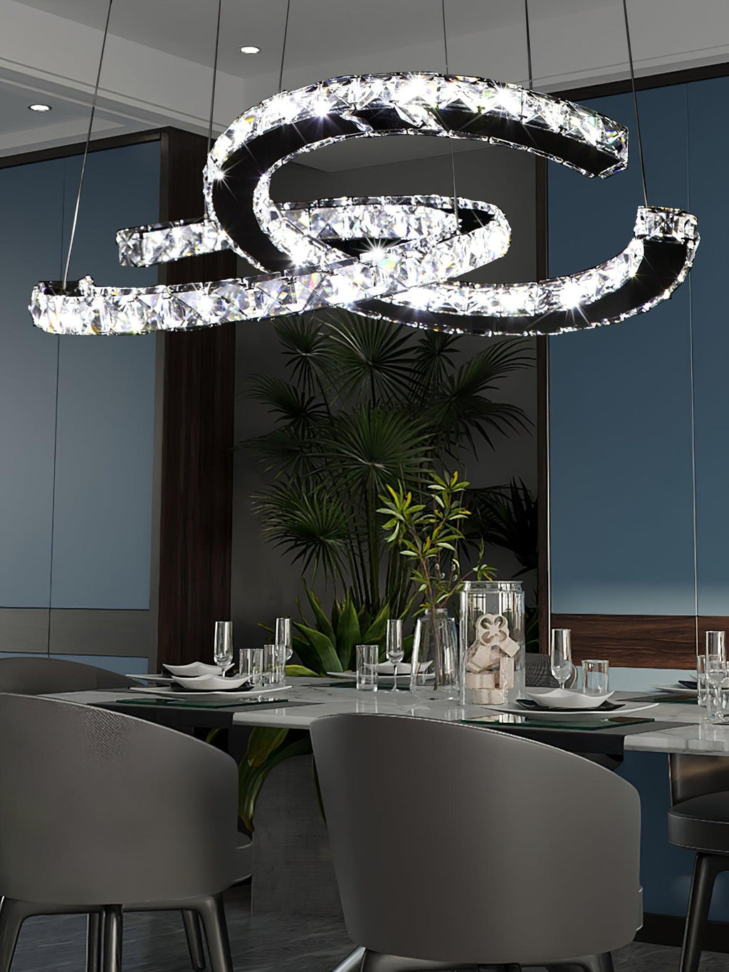 Clear-crystal Clérachic pendant above a dark dining table with grey chairs, glasses and a leafy plant.