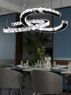 Clear-crystal Clérachic pendant above a dark dining table with grey chairs, glasses and a leafy plant.