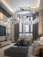 Clérachic crystal pendant lit in a high-ceilinged living room with a television, cream sofas and tall curtains.