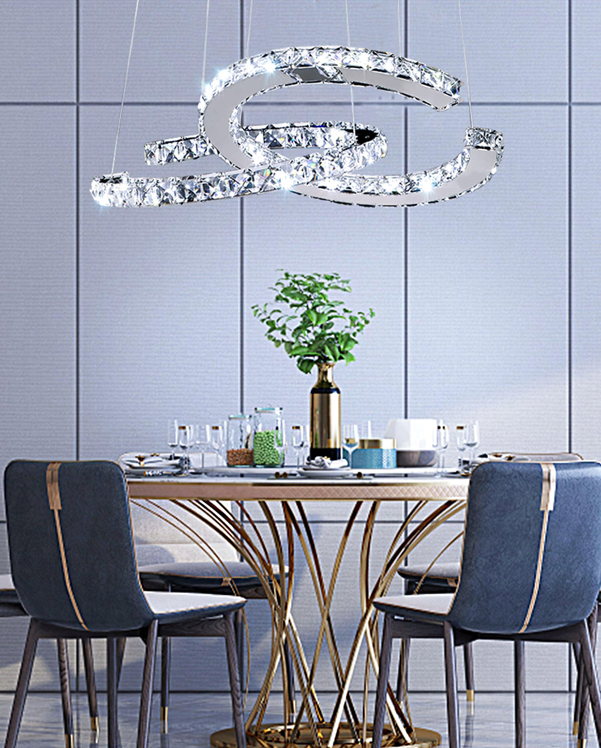 Clear Clérachic crystal pendant above a round gold-based dining table with navy chairs, glasses and a plant.