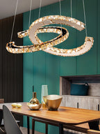 Clérachic crescent pendant with cognac-toned crystals above a wooden table with gold bowls, against a teal wall.