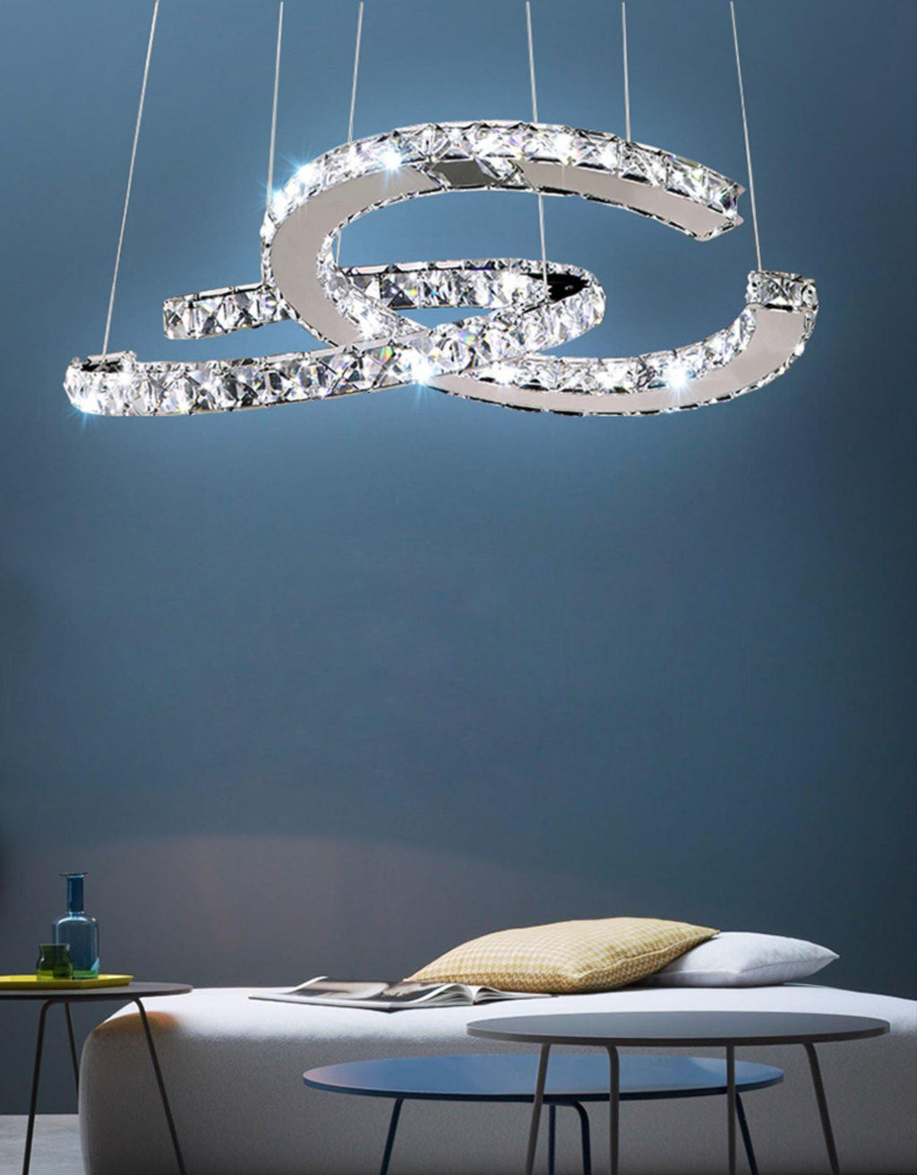 Clear-crystal Clérachic pendant lit against a blue wall above a low sofa and a pair of round side tables.